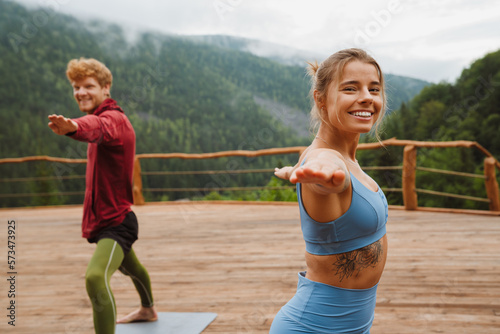 Young white man and woman practicing yoga on fitness mats in forest