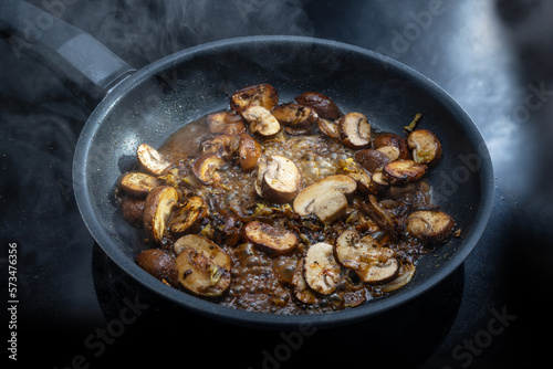 Mushrooms with sauce are cooked in a steaming black frying pan on the cooktop, preparing a vegetarian meal, copy space, selected focus