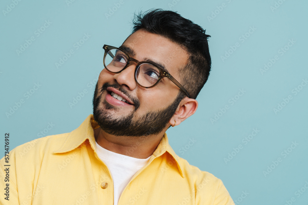 Obraz premium Smiling indian guy looking away while posing isolated over blue wall