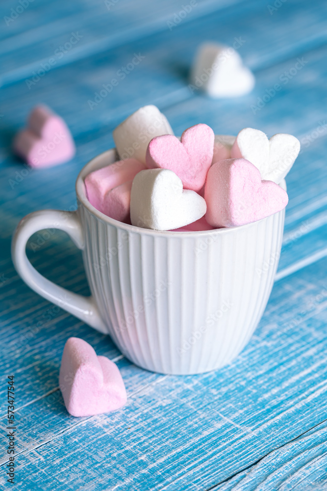 A cup with heart-shaped marshmallows, close-up on a blue wooden background. A cup with heart-shaped marshmallows, close-up on a blue wooden background.