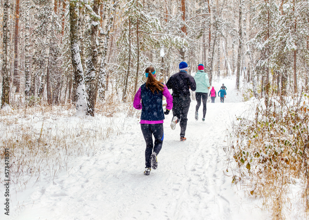 back group runners run winter trail race in forest during a snowfall