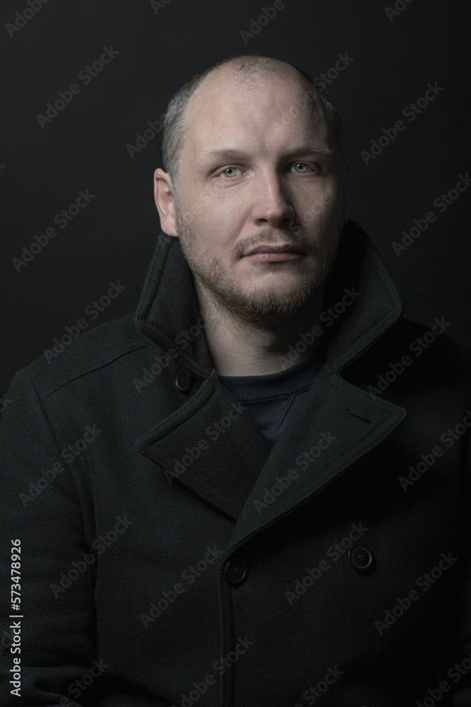 Lifestyle, fashion, occupation concept. Man with black coat studio portrait. Model with beard looking at camera with serious look. Dark studio background. Toned image with gray color