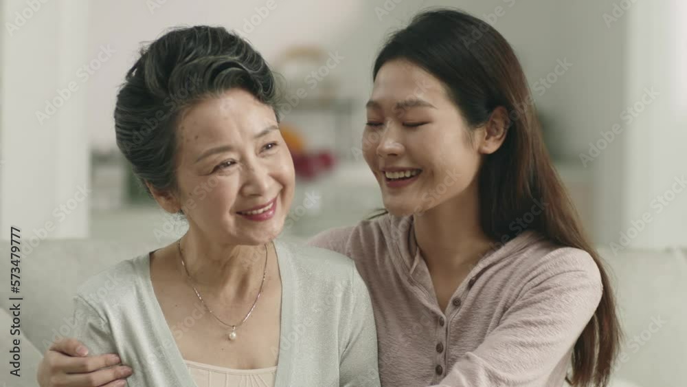 young asian adult daughter and senior mother sitting on couch relaxing in living room at home young asian adult daughter and senior mother sitting on couch relaxing in living room at home