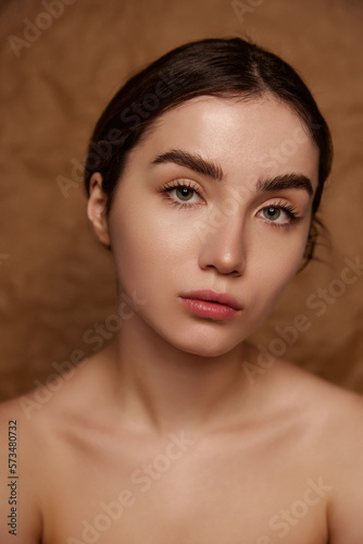 No makeup look. Beautiful young brunette girl with healthy smooth well-kept skin over brown studio background. Concept of natural beauty  skincare  cosmetology  plastic surgery  health