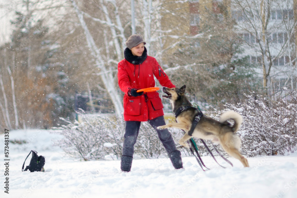Girl playing with dog in snow in winter time with snowflakes in air. Selective focus
