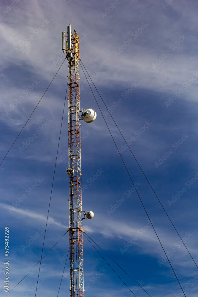 Telecommunication tower with radio, microwave and television antenna system located in the forest against the blue sky. Antenna tower, view from the ground Telecommunication tower with radio, microwave and television antenna system located in the forest against the blue sky. Antenna tower, view from the ground