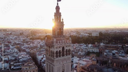 Aerial dolly out revealing Giralda tower in the famous European cathedral of Seville with scenic sunlight behind photo
