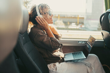 One woman listening music with headphones and computer sitting inside public bus transport enjoying travel transportation trip. Modern traveler. Happy free female people enjoying laptop device for job