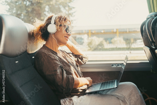 Foto Modern travel lifestyle people with happy smiling woman listening music with headphones and laptop computer sitting and relaxing on a bus seat as a travel passenger
