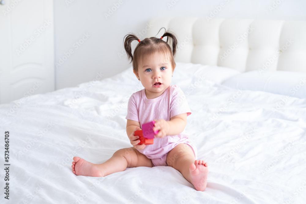 funny baby girl in pink bodysuit playing with children wooden cubes toys on bed funny baby girl in pink bodysuit playing with children wooden cubes toys on bed