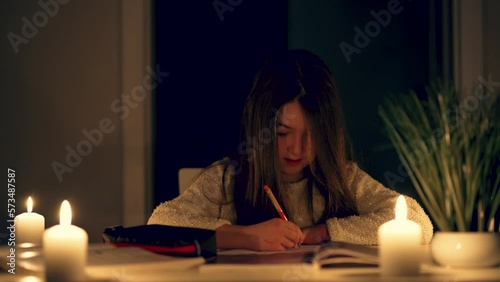 Poor young rural girl from informal settlement writing and learning lessons by candlelight. Children doing school homework at home. Studying without electricity photo