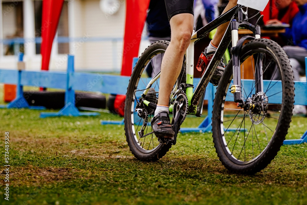 Fototapeta premium legs young cyclist riding mountain bike on field of green grass