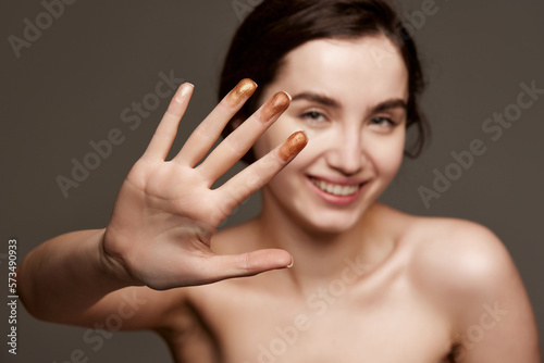 Sparkling nude eyeshadow swatches on fingers. Portrait of young beautiful girl with brown hair posing over dark grey studio background. Concept of natural beauty  skincare  cosmetology  cosmetics