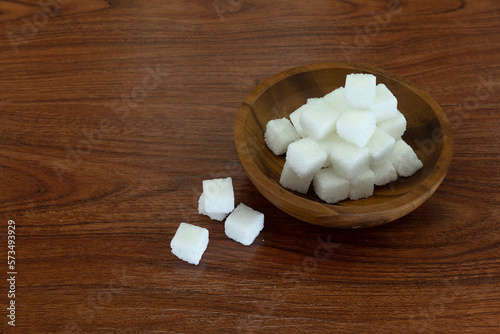 Sugar cubes in wooden bowl on wooden texture background.