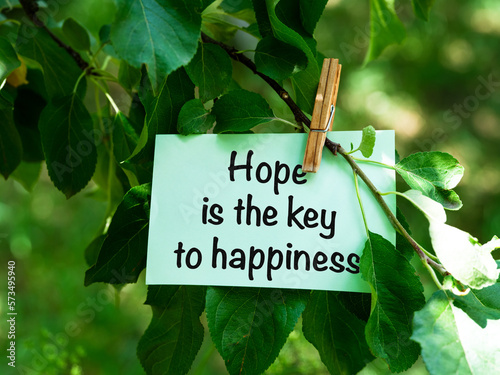 A green paper note with words Hope is the Key to Happiness hanging on a tree branch. © rosinka79