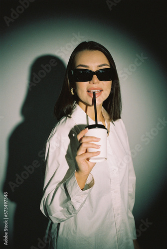A young woman drinks coffee on a white background. Fashion shooting in the studio. Film photography  noise. Weak depth of field