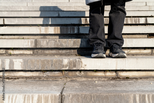 Photography legs in pants and sneakers on concrete steps outdoors. Person and concrete stairs, urban style.