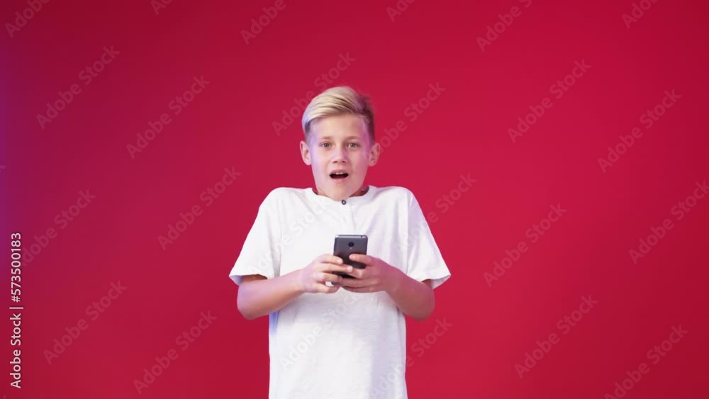 Successful result. Excited boy. Digital technology. Happy surprised teenager kid playing smartphone on red background. Successful result. Excited boy. Digital technology. Happy surprised teenager kid playing smartphone on red background.