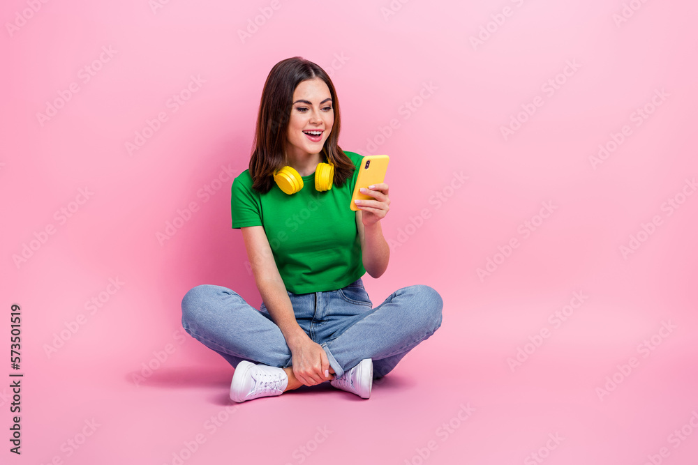 Full body portrait of pretty excited lady sit floor use smart phone chatting isolated on pink color background Full body portrait of pretty excited lady sit floor use smart phone chatting isolated on pink color background