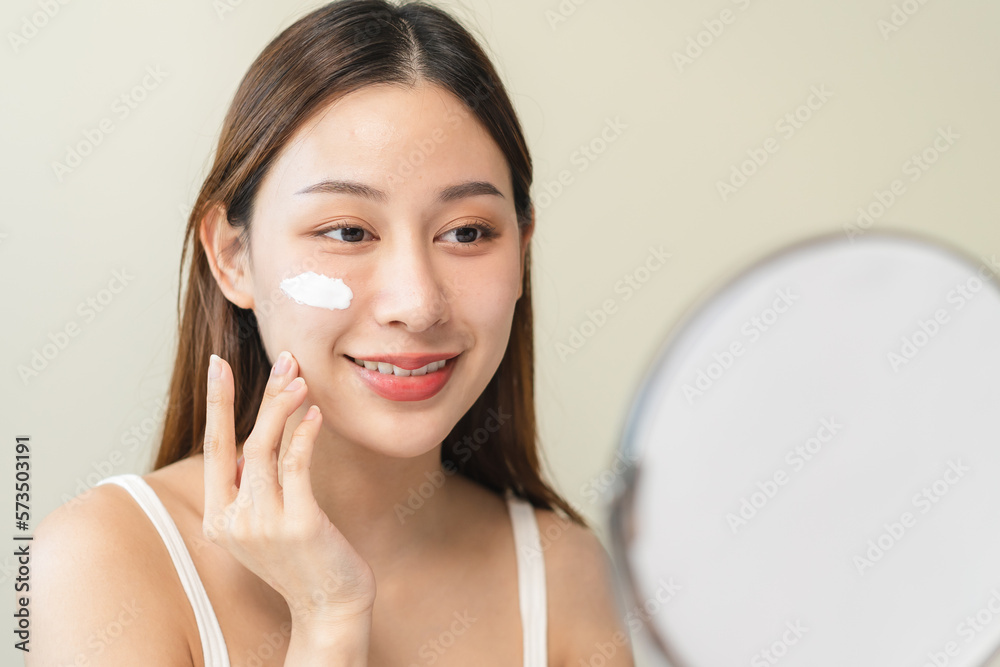 wellness care concept, young woman looking at the mirror and applying facial skin care cream on her face wellness care concept, young woman looking at the mirror and applying facial skin care cream on her face