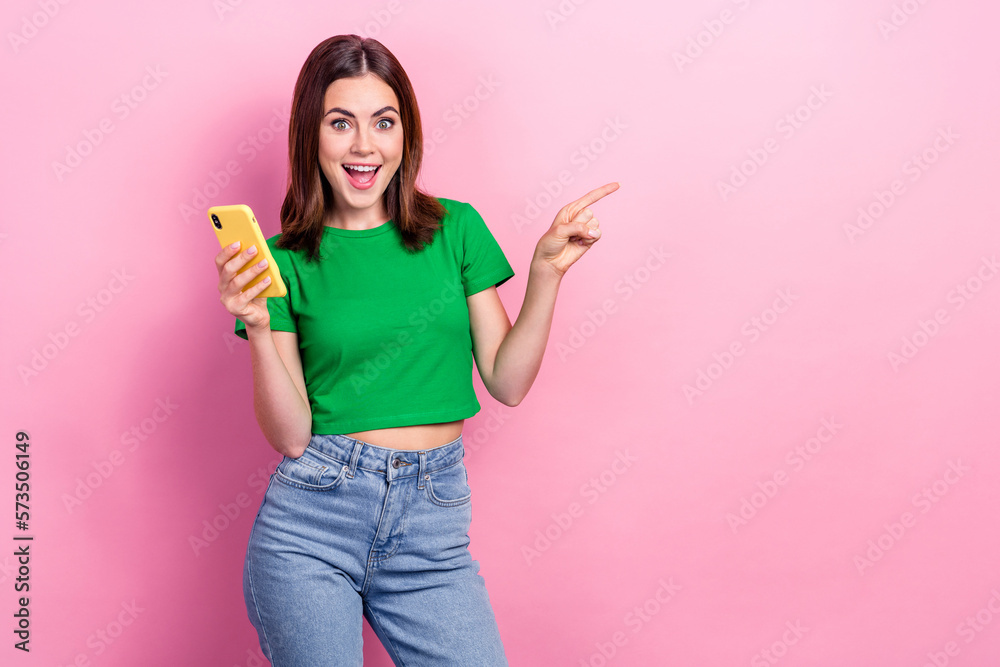 Portrait of astonished charming blogger girl hold smart phone direct finger empty space promo isolated on pink color background Portrait of astonished charming blogger girl hold smart phone direct finger empty space promo isolated on pink color background