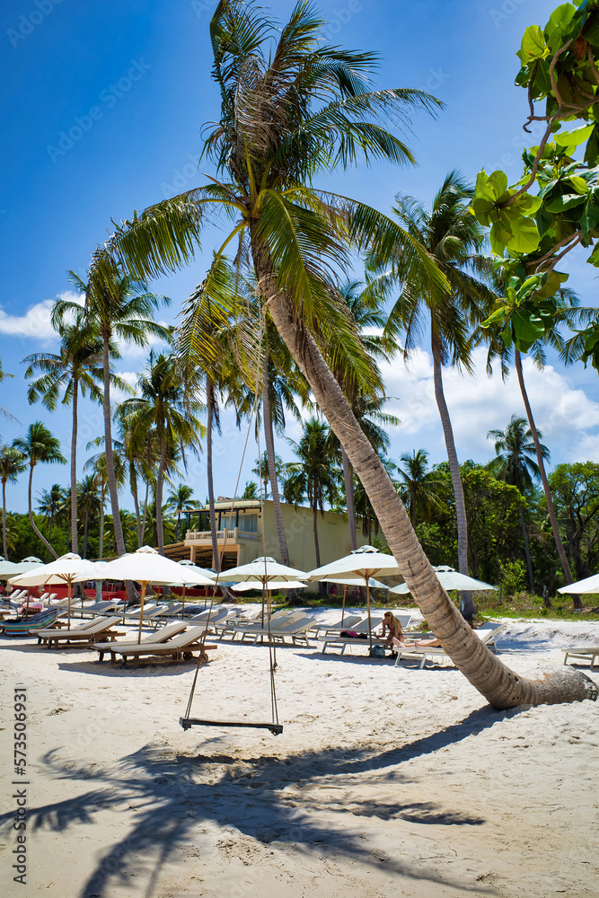 Phu Quoc island, Vietnam - March 31, 2019: Swing on a palm tree. Sea beach in the afternoon, clear sky. Spa Romance