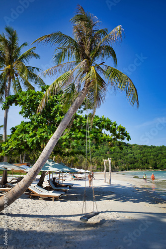 Obraz na płótnie Phu Quoc island, Vietnam - March 31, 2019: The beach is snow-white, overhanging palm trees with swings. Vacationers tourists under the beach umbrellas. Beautiful seashore. w salonie