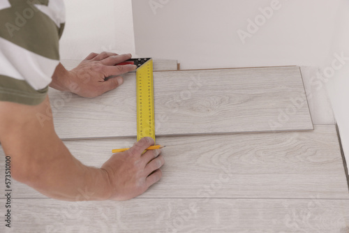 Professional worker using measuring tape during installation of laminate flooring indoors  closeup