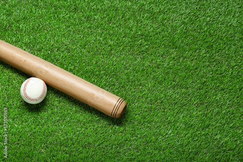 Wall Mural Wooden baseball bat and ball on green grass, flat lay