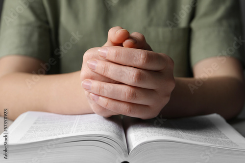 Woman holding hands clasped while praying over Bible at table, closeup