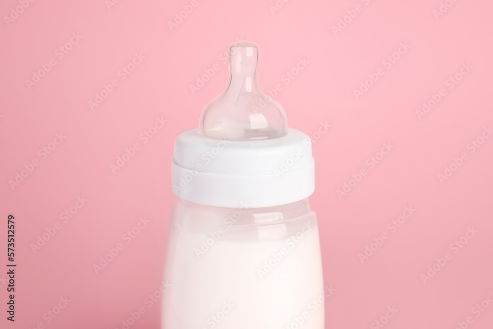 One feeding bottle with milk on pink background, closeup One feeding bottle with milk on pink background, closeup