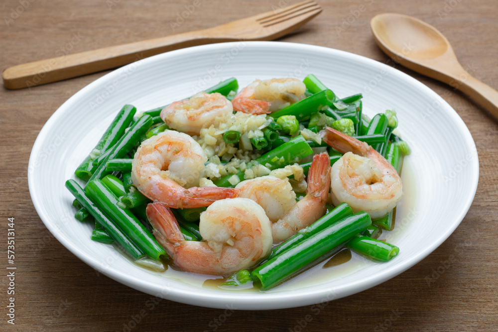 close up of stir fried shrimp with onion flower stem in a ceramic dish on wooden table. asian homemade style food concept.