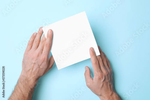 Man holding sheet of paper on light blue background, top view. Mockup for design