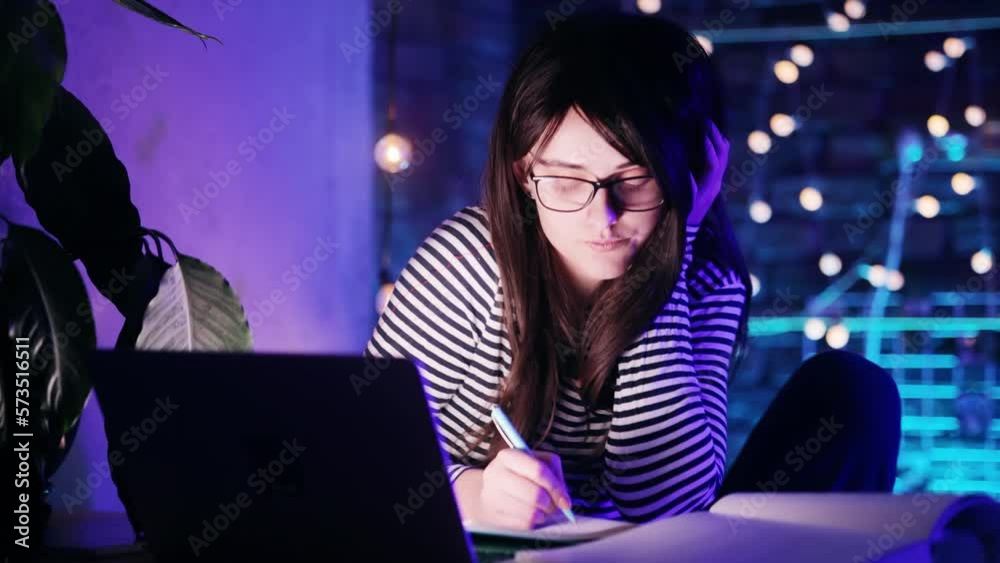 Sleepy girl with laptop screen light on face exhausted from remote distance education and hard program late take break for scrolling feed in social media texting browsing on smartphone at late night Sleepy girl with laptop screen light on face exhausted from remote distance education and hard program late take break for scrolling feed in social media texting browsing on smartphone at late night