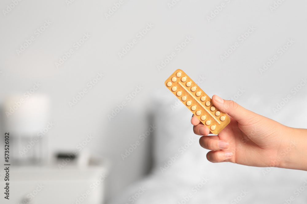 Fototapeta premium Woman holding blister of oral contraception pills against blurred background, closeup. Space for text