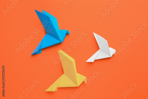 Beautiful colorful origami birds on orange background, flat lay