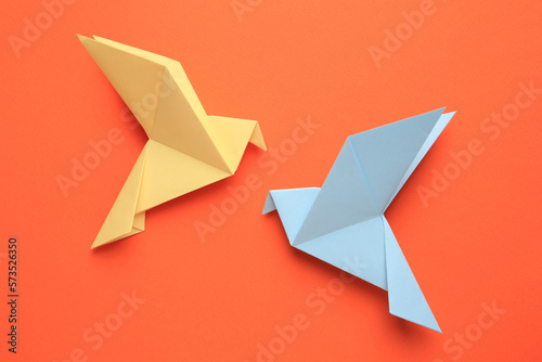 Beautiful colorful origami birds on orange background  flat lay