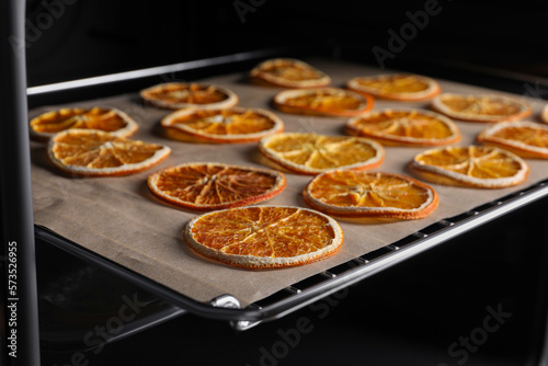 Many dry orange slices on parchment paper in oven