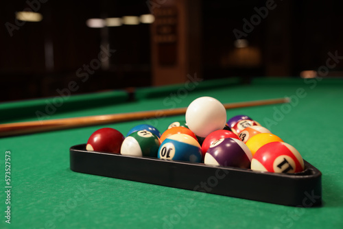 Plastic triangle rack with billiard balls and cue on green table indoors, space for text
