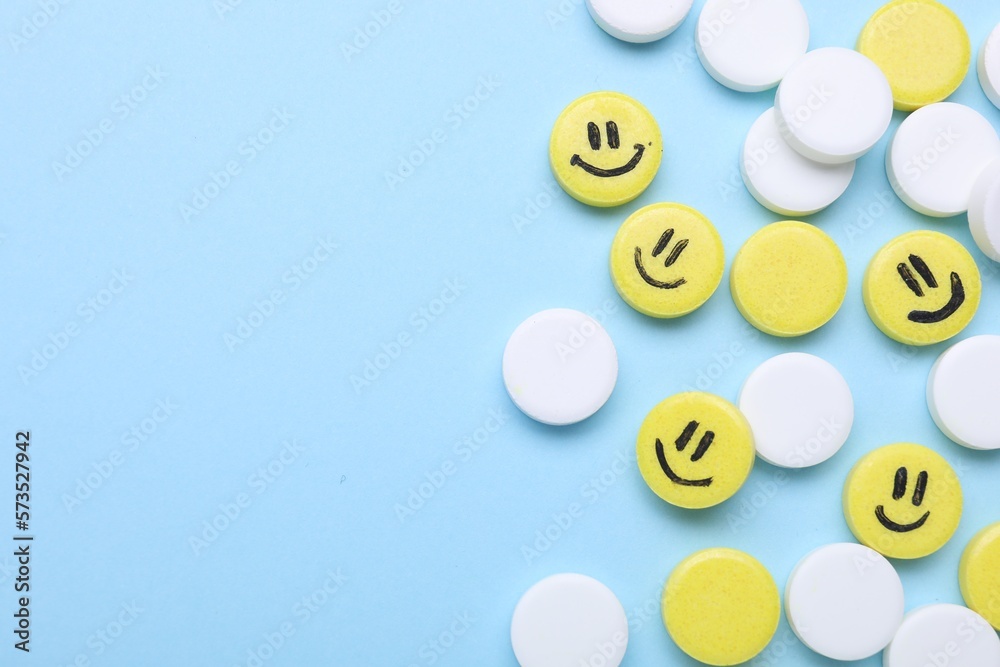 Many antidepressant pills with happy faces on light blue background, flat lay. Space for text
