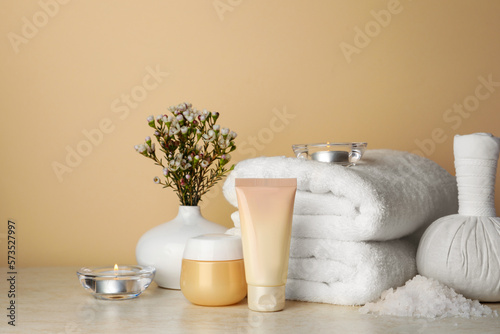 Composition with different spa products, candles and flowers on beige table. Space for text