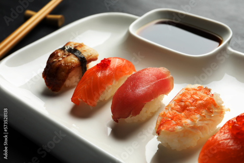 Plate with delicious nigiri sushi and soy sauce on black table, closeup