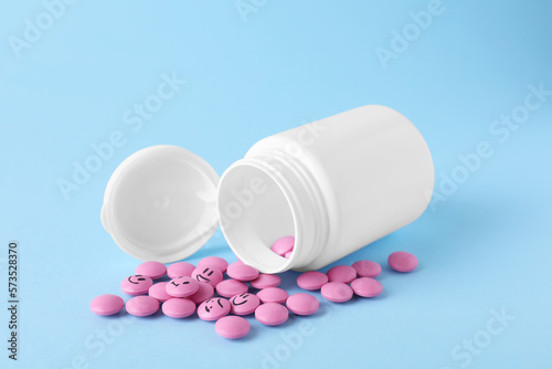 Pink antidepressants with emoticons and medical jar on light blue background
