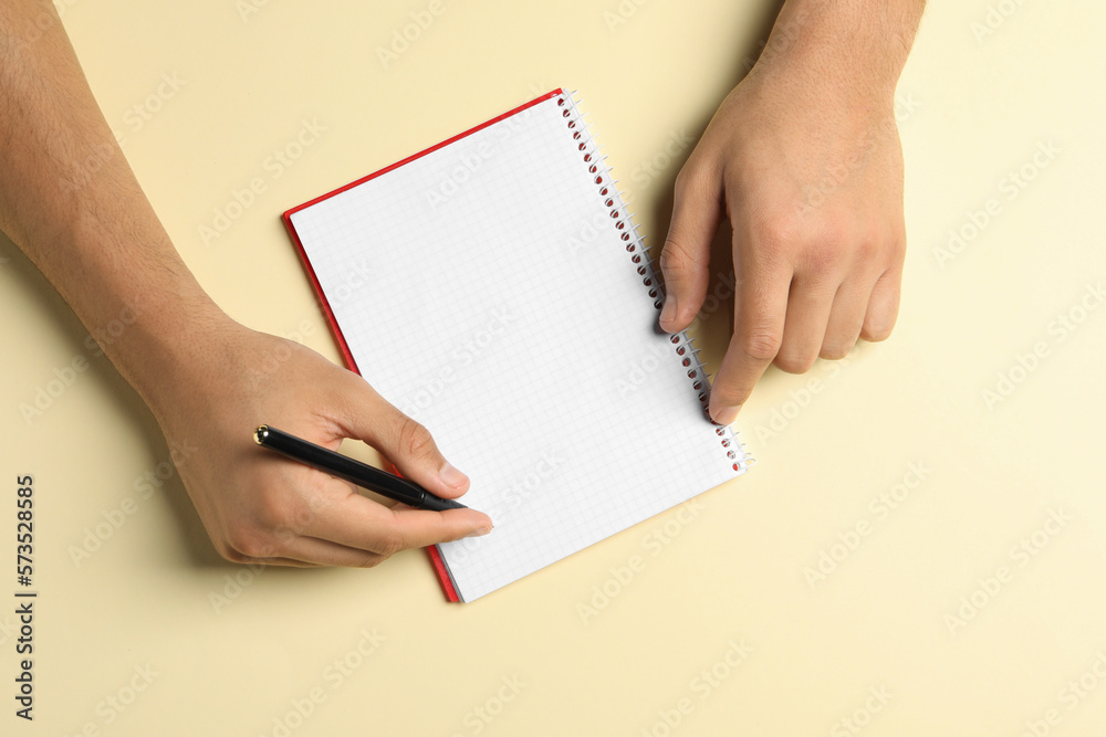 Man with pen and notepad on pale yellow background, top view Man with pen and notepad on pale yellow background, top view