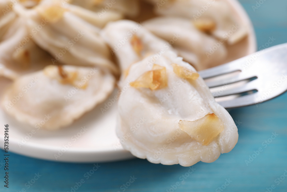 Fork with delicious dumpling (varenyky) at light blue table, closeup