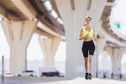 Fit young brunette tanned woman running under overpass, training outdoor. Gorgeous hispanic girl in yellow bra and black leggings happy to be healthy and successful. Healthy lifestyle. Female runner. © Iona