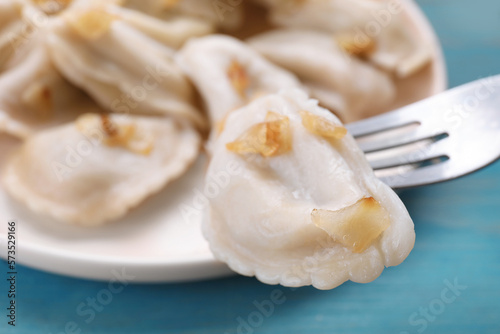 Fork with delicious dumpling (varenyky) at light blue table, closeup