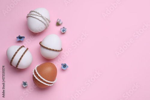Beautifully decorated Easter eggs and flowers on pink background, flat lay. Space for text