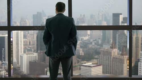 Fotografie Man with hands in the pocket look out window and admire sky scraper view, power
