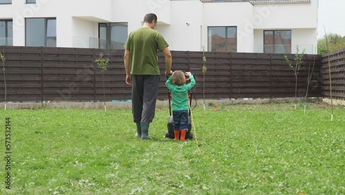 Father and son son with back hold together lawn mower work in garden, kid lean